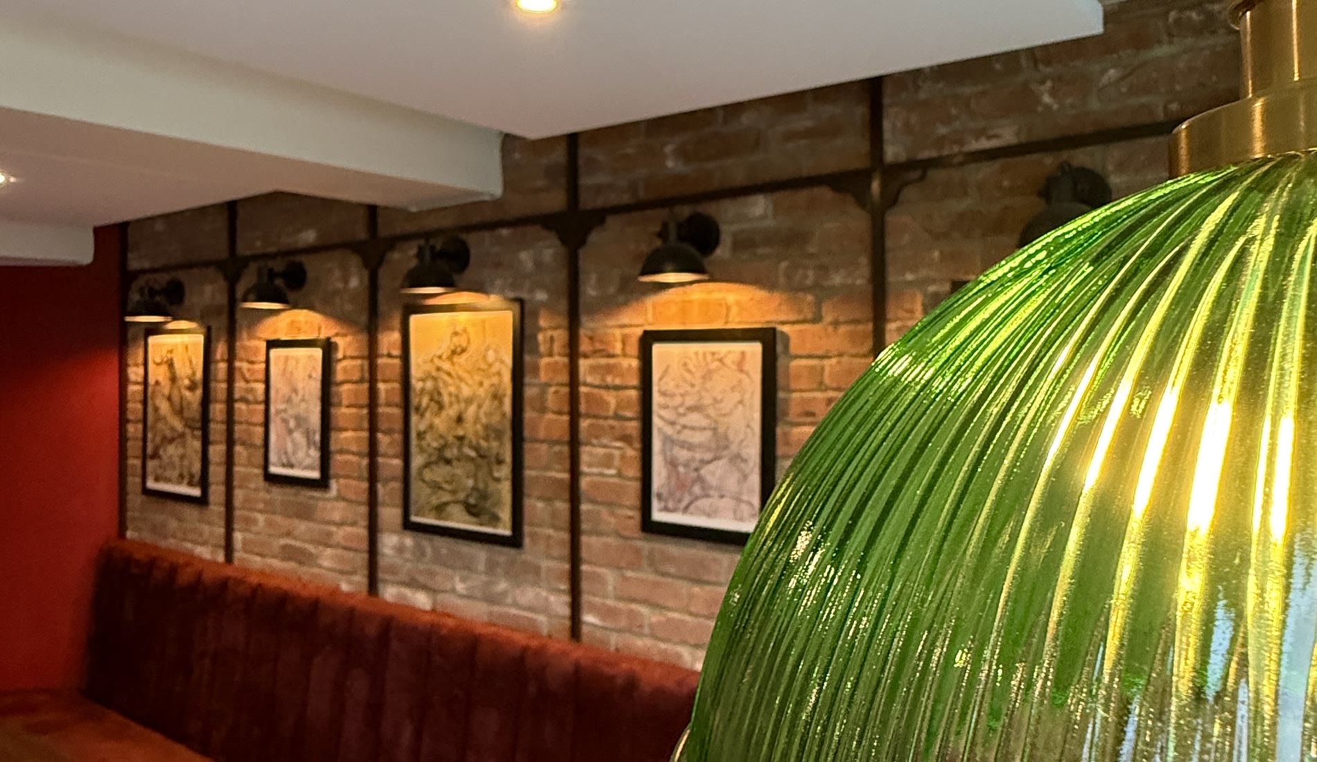 The dining room: exposed brick under black wall lights, with a long burgundy velvet banquette running the length of it.
