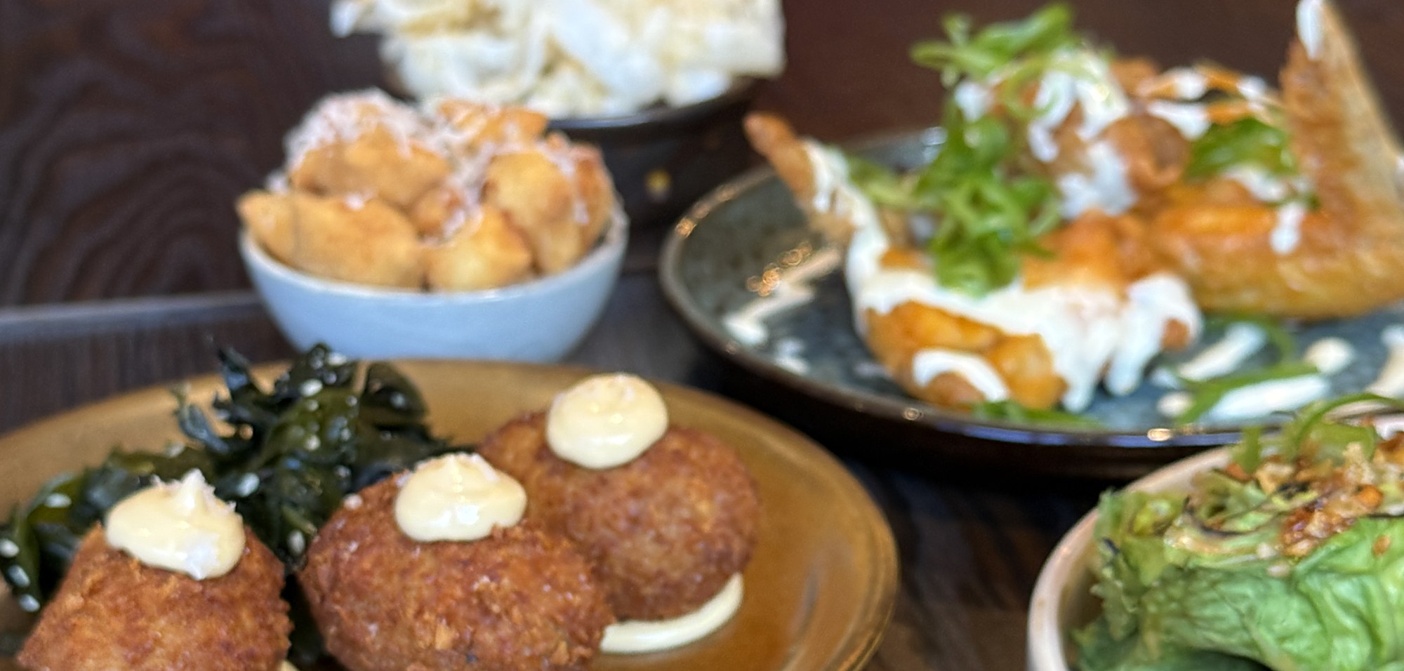 Looking down on a full table: fried chicken, sticky wings, salt-and-pepper pieces, slaw, pickles and a platter of croquettes.